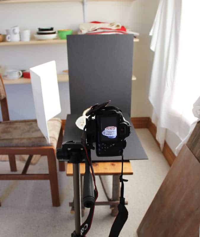 A view of behind a camera on a tripod that is photographing a cake.
