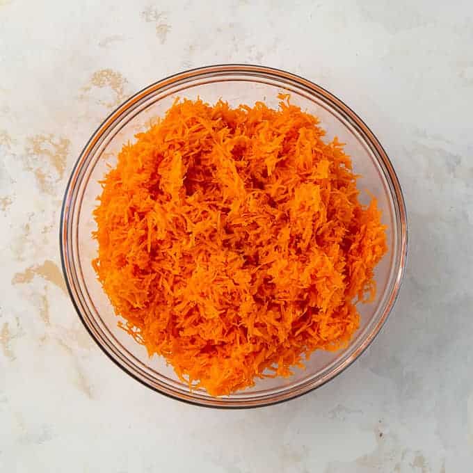 Overhead view of grated carrots in a clear glass bowl.