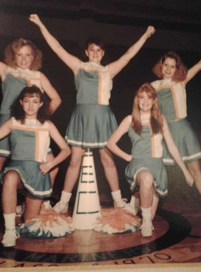 Five young female cheerleaders in uniform. Three are standing in back and two are kneeling in front.