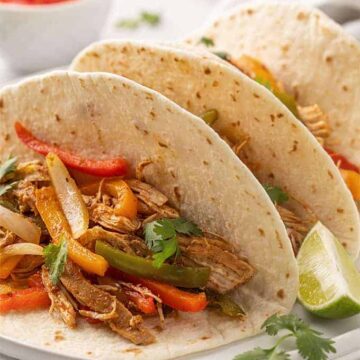 Three chicken fajitas on a white plate beside a lime wedge