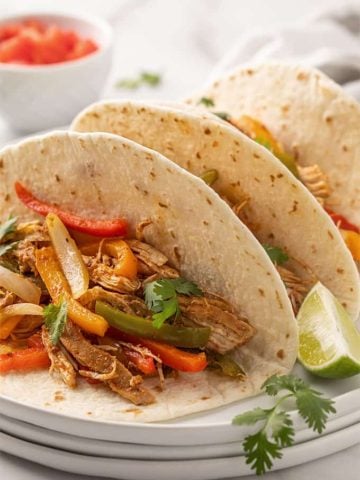 Three chicken fajitas on a white plate beside a lime wedge