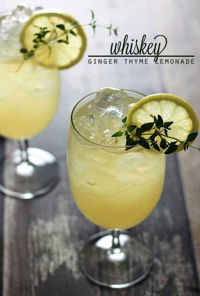 Two lemonade cocktails garnished with lemon and fresh thyme on a wood surface.