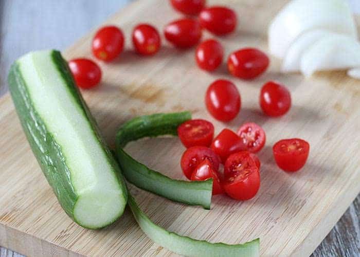 A partially peeled cucumber and halved cherry tomatoes on a wood cutting board.
