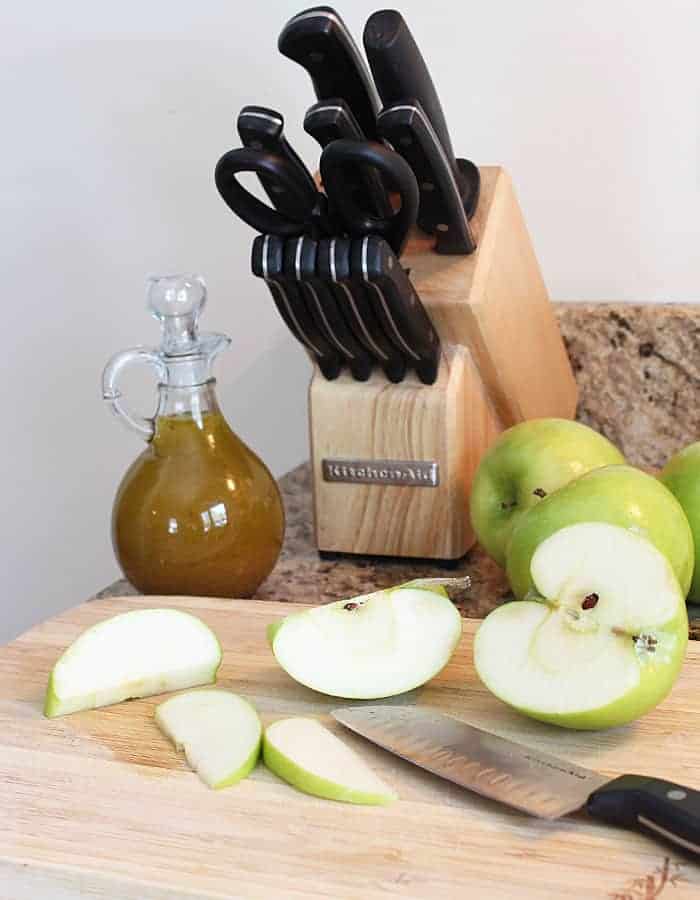 Sliced Granny Smith apples on a wood cutting board with a knife.