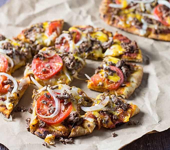 Closeup view of pizza with ground beef, tomatoes, onions and cheese on naan flatbread.