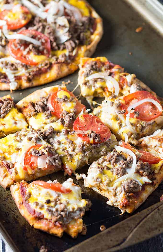 Cheeseburger flatbread pizza sliced into squares on a baking sheet.
