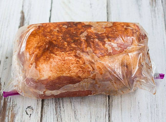 A seasoned raw pork shoulder in marinade in a resealable plastic bag.