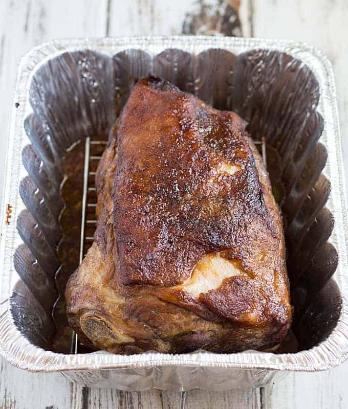 A cooked pork shoulder on a shallow rack in a disposable aluminum pan.