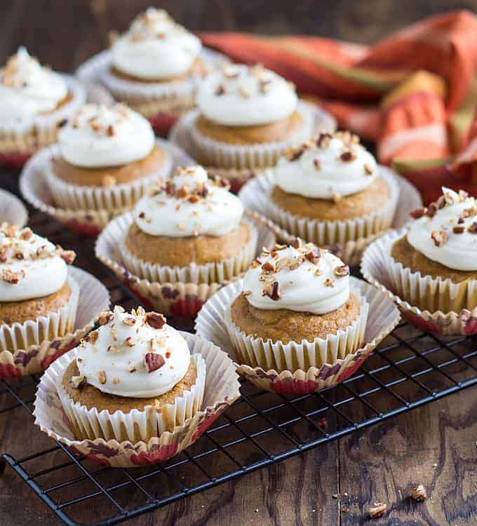 Cupcakes topped with cream cheese frosting and chopped pecans on a baking rack.