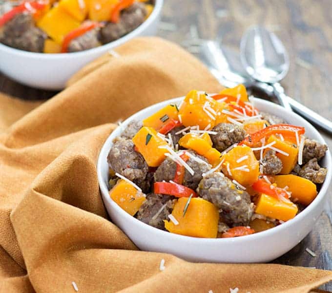 Crumbled sausage, squash and vegetables in a white bowl beside an orange napkin and two spoons.