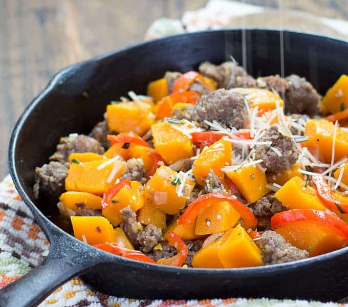 Grated Parmesan cheese being sprinkled on squash, sausage and vegetables in a cast iron skillet.