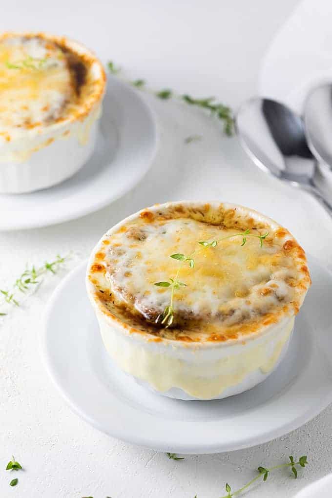 A bowl of onion soup topped with melted provolone cheese and a sprig of thyme.