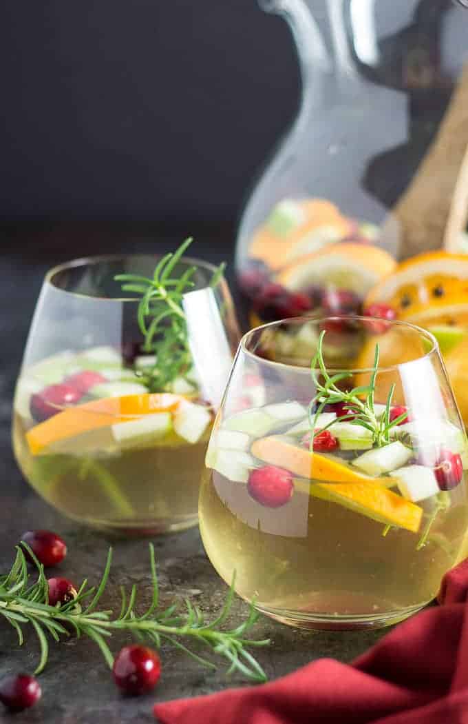 Two glasses of white sangria with cranberries, oranges, apples and fresh rosemary.