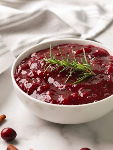 Cranberry sauce from scratch in a white bowl garnished with a sprig of rosemary