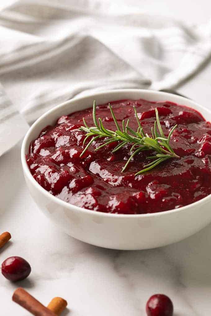 Cranberry sauce from scratch in a white bowl garnished with a sprig of rosemary.