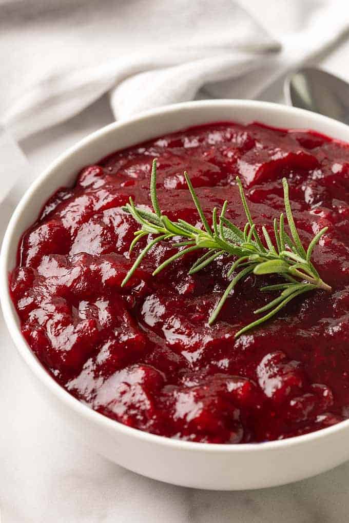 Closeup of cranberry sauce garnished with a sprig of rosemary in a white bowl.