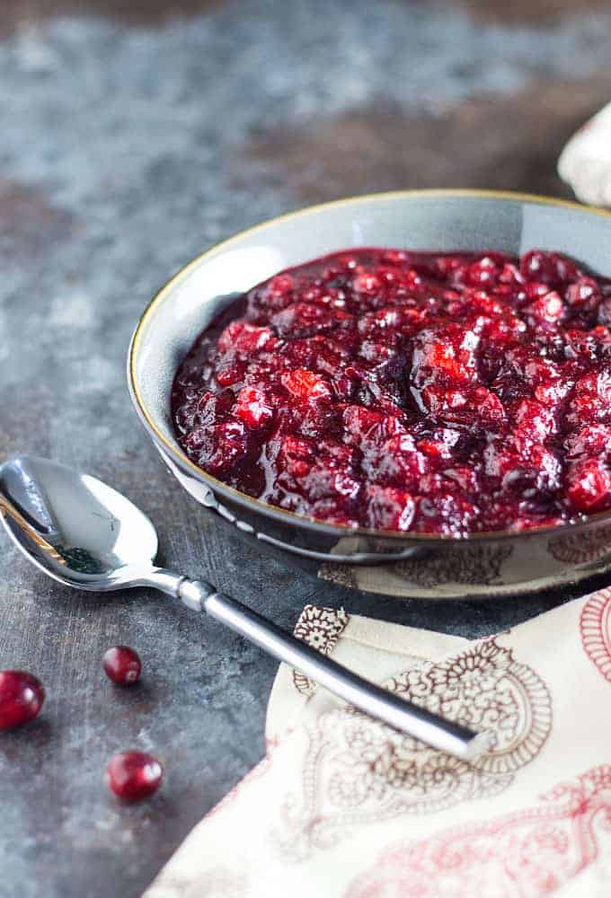 Cranberry sauce in a gray and brown bowl beside a spoon and a patterned napkin.