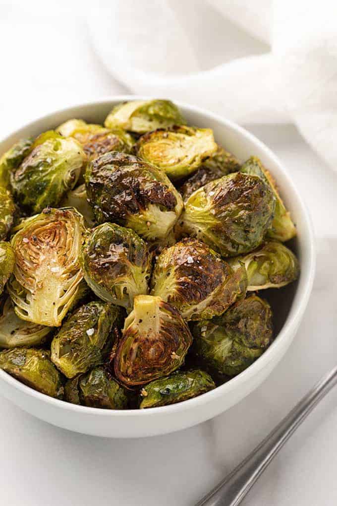 Roasted Brussels sprouts with garlic in a white bowl on a marble surface