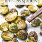 Oven roasted Brussels sprouts on a baking sheet with a spatula. Overlay text at top of image.
