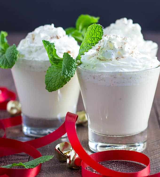 Closeup view of three cocktails by red holiday ribbon and small decorative bells.