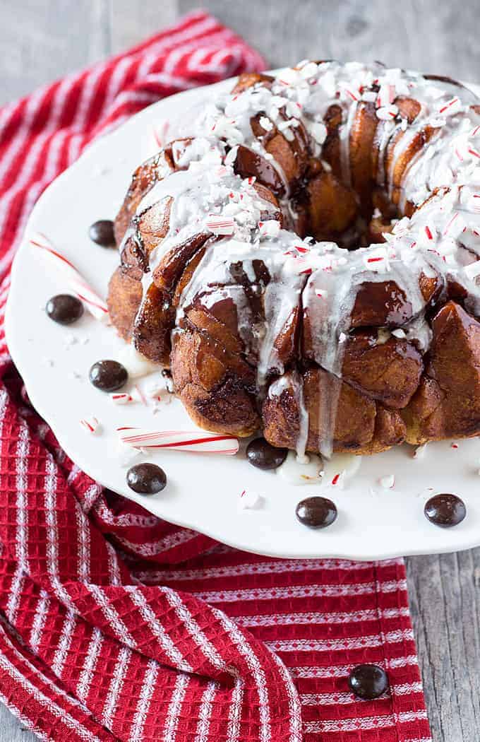 Monkey bread topped with a white glaze and crushed peppermint on a round white plate.