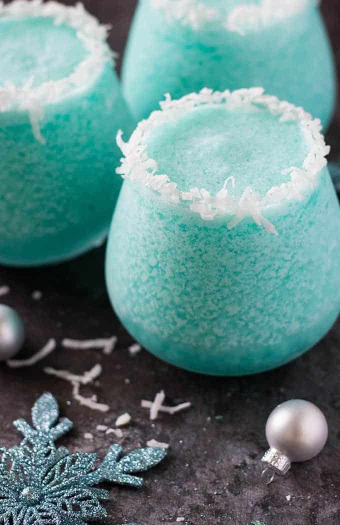 Closeup of three frozen blue cocktails by a decorative snowflake and holiday ornament.
