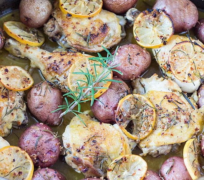 Closeup view of chicken with red potatoes and lemon slices topped with a sprig of rosemary.