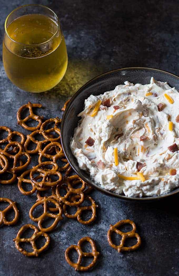 Overhead view of dip in a blue bowl by pretzels and a glass of beer.