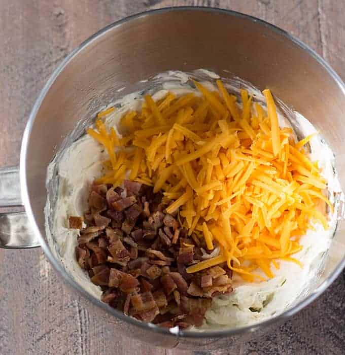 Overhead view of cream cheese, shredded cheddar cheese and bacon pieces in a stainless bowl.