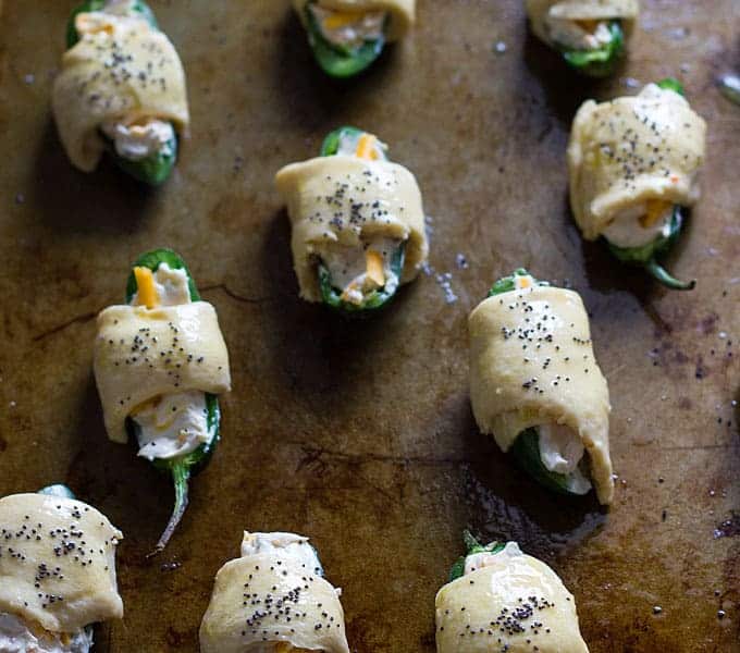 Overhead view of halved jalapenos wrapped in crescent rolls, brushed with egg and sprinkled with poppy seeds.