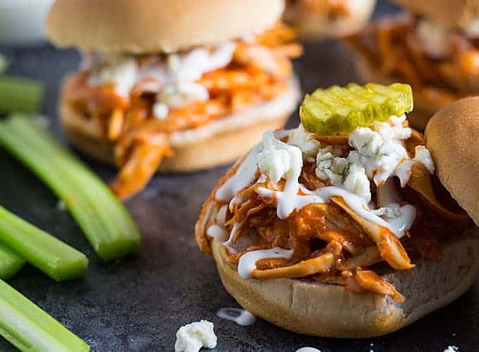 Closeup view of a slider roll topped with buffalo chicken, ranch dressing, blue cheese and a sliced pickle.