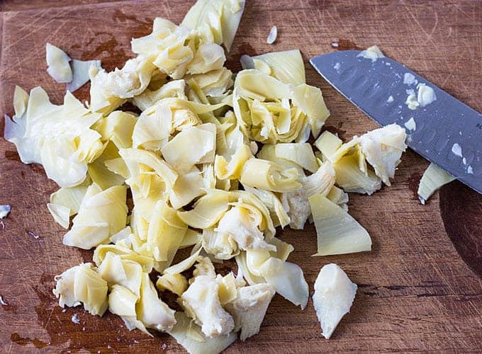 Roughly chopped canned artichoke hearts beside a knife on a cutting board.