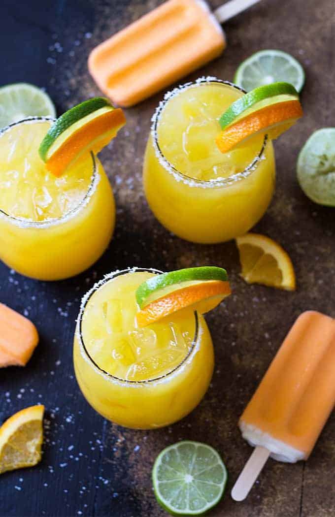 Overhead view of three garnished orange margaritas surrounded by creamsicle ice cream pops.