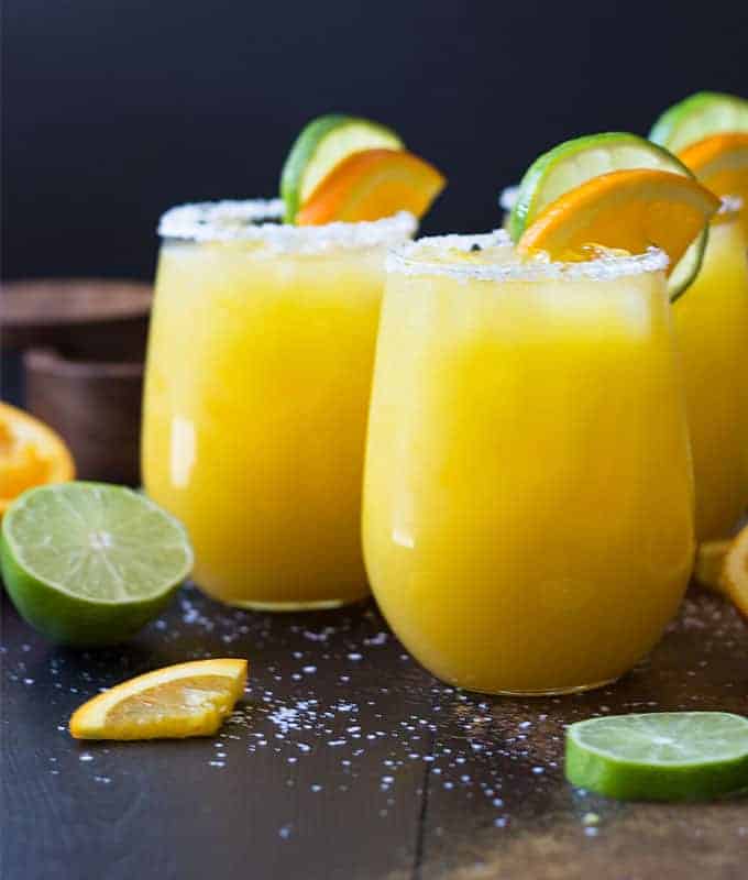 Front view of three orange margaritas garnished with orange and lime.