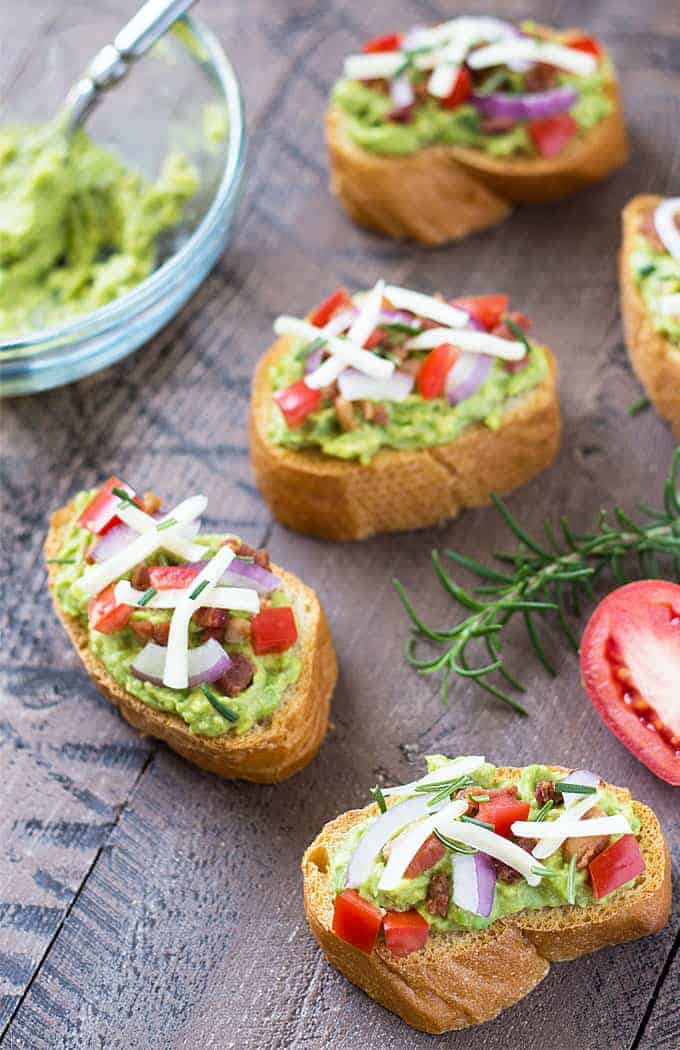 Toasted French bread slices topped with an avocado mixture, bacon, cheese and vegetables.