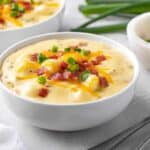 Potato Soup garnished with bacon, cheese and green onions in a round white bowl
