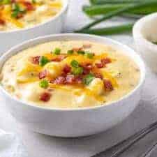 Potato Soup garnished with bacon, cheese and green onions in a round white bowl