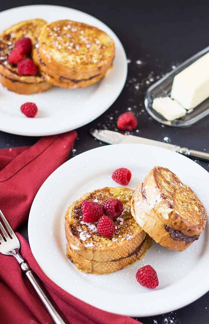 Overhead view of French toast topped with raspberries on two white plates.
