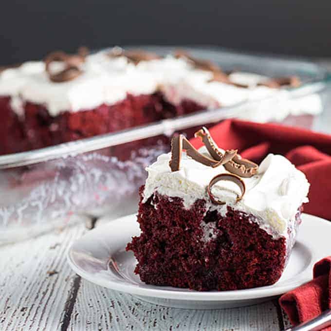 A slice of red velvet cake on a white plate by a red napkin.