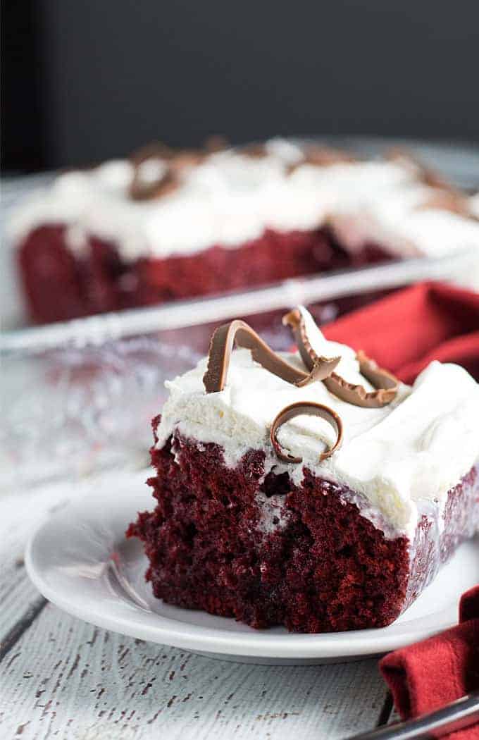 A slice of red velvet cake frosted with whipped cream and topped with chocolate shavings.