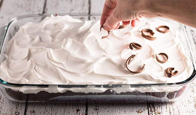 Topping a cake that has been frosted with whipped cream with chocolate shavings.