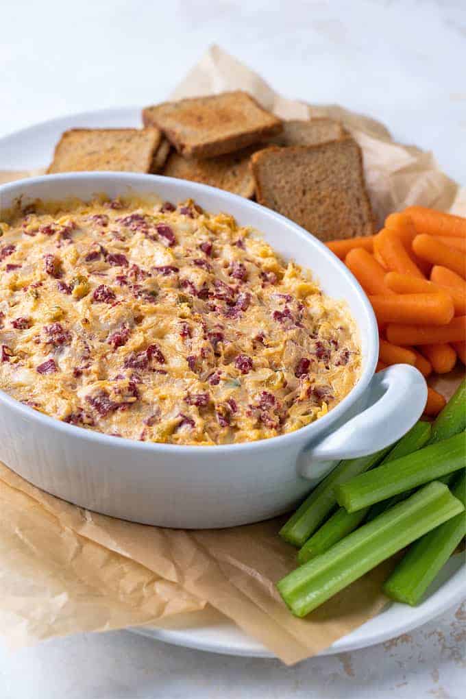 Baked Reuben Dip in an oval white baking dish with toasted rye bread and vegetables 