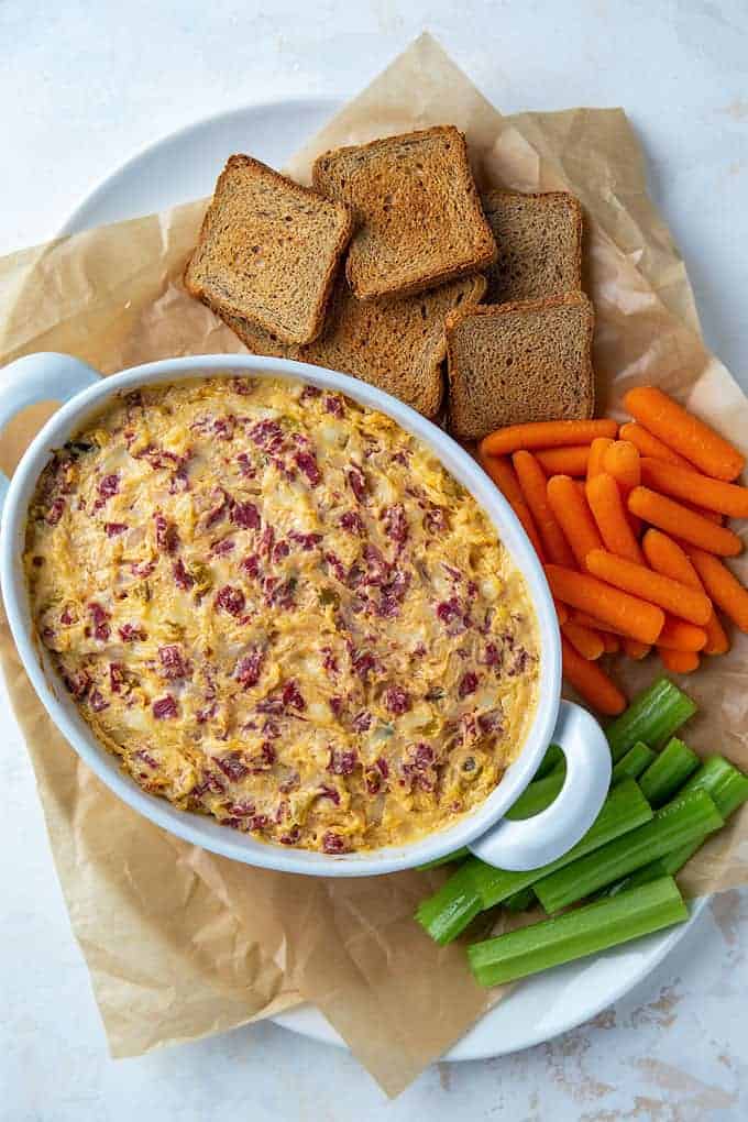 Overhead view of cheesy Reuben dip on a serving platter with veggies and rye toast