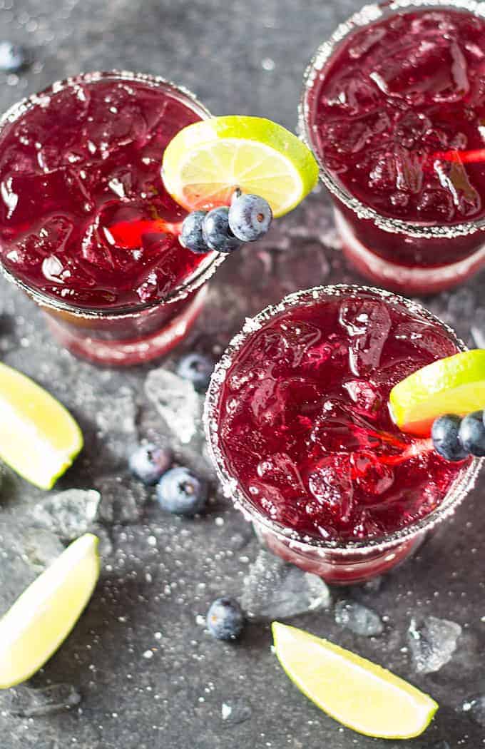 Overhead view of 3 blueberry margaritas - Each garnished with lime and a skewer of blueberries.