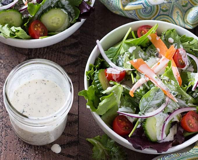 Overhead view of a jar of dressing by a salad in a bowl topped with dressing.