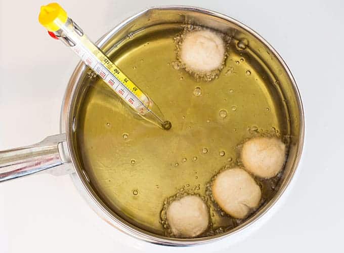 Overhead view of a pot of vegetable oil with donut holes and a candy thermometer.