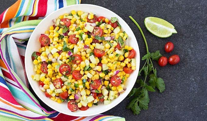 Overhead view of corn salad in a round white bowl by a striped napkin.