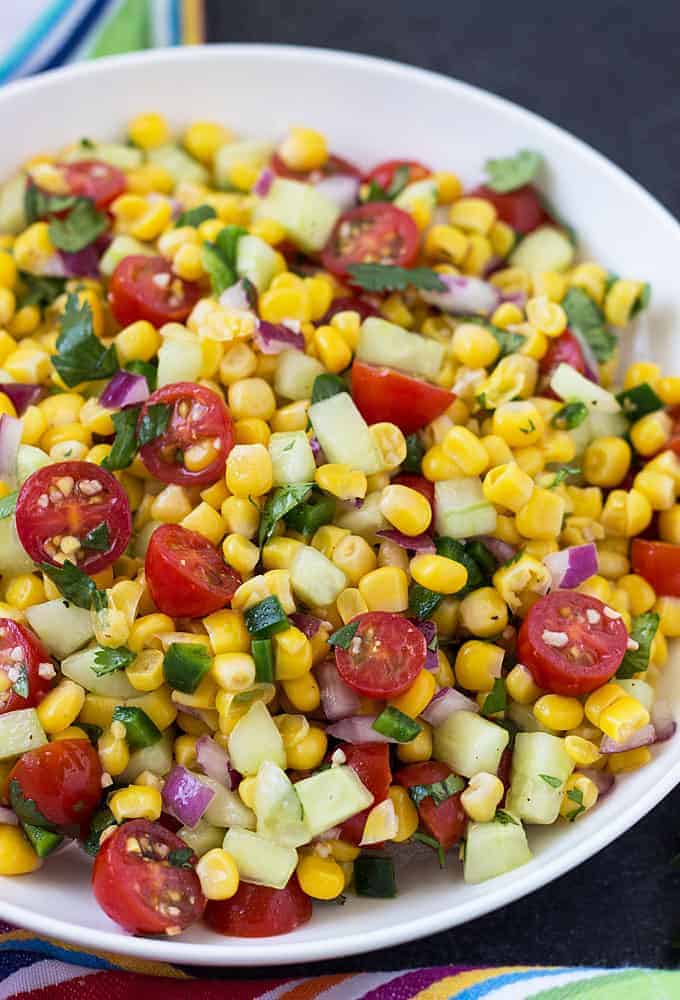 Closeup view of corn and tomato salad with cucumbers, red onion and jalapeno in a white bowl.