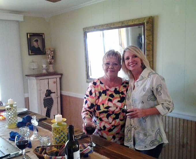 A young woman and her mother standing beside a kitchen table smiling.
