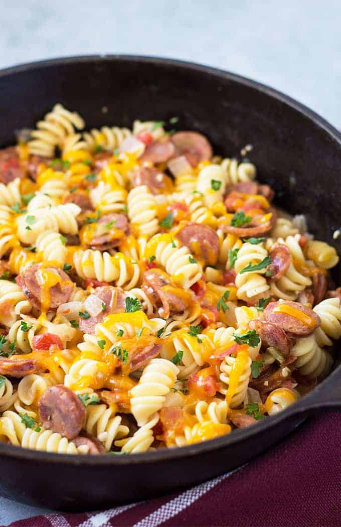 Closeup view of cheesy rotini pasta with sliced andouille sausage in a skillet.